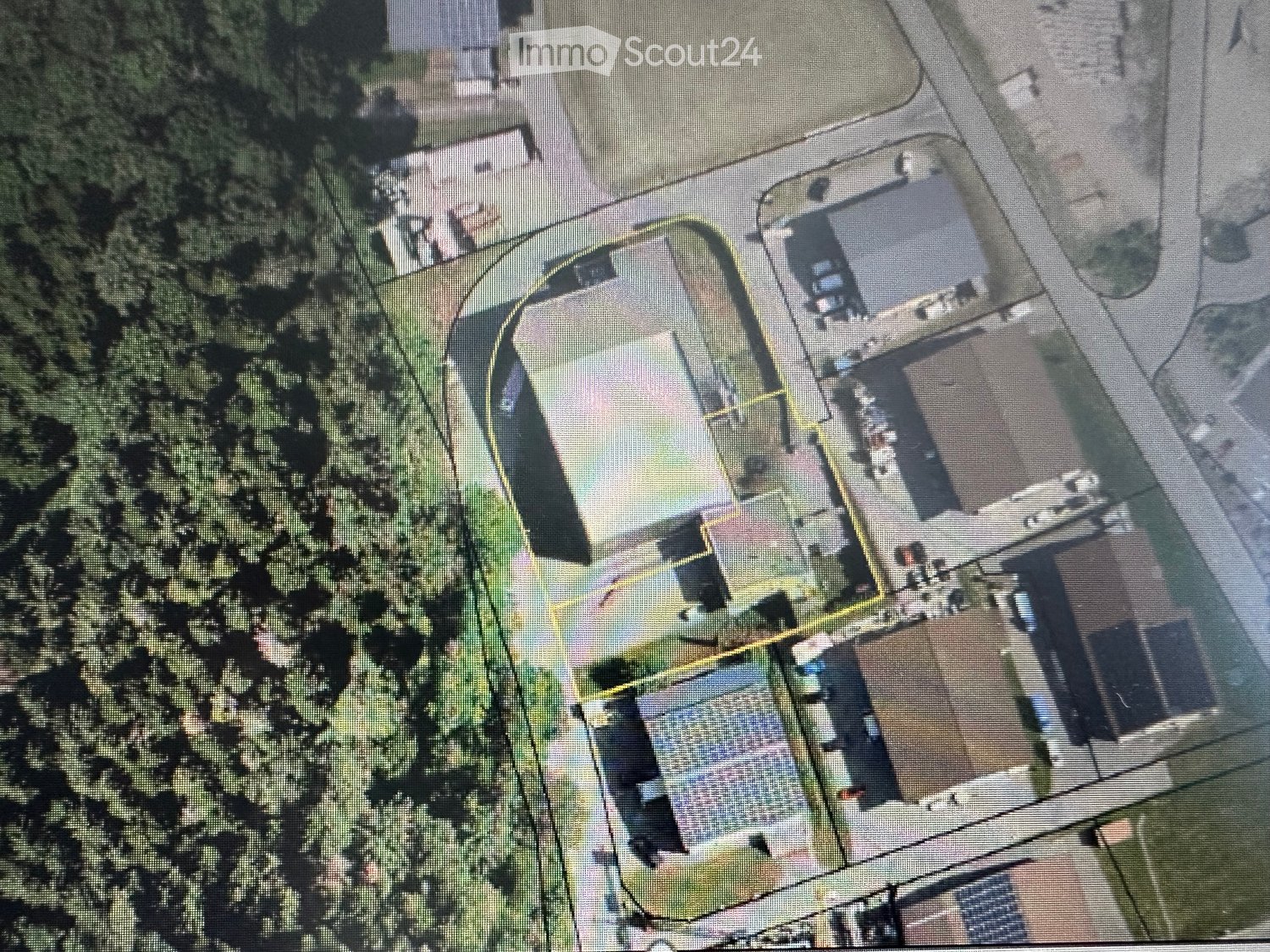 Aerial view of a residential property with multiple buildings, including a main house, garage, and outbuildings, surrounded by trees and a driveway.