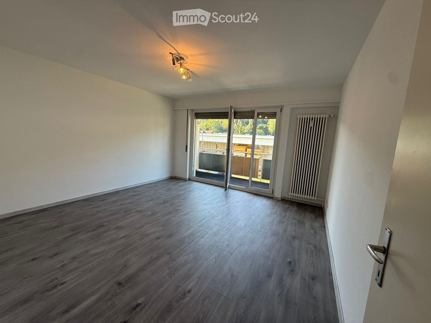 Empty room with wooden flooring, white walls, and a sliding glass door leading to a balcony area.