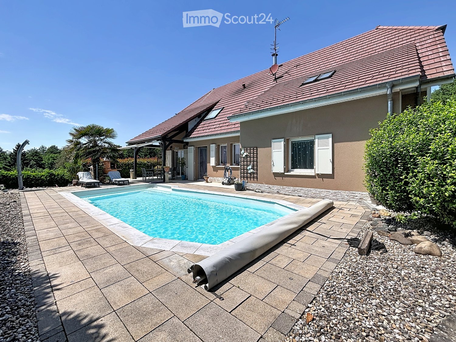 Outdoor area with a swimming pool, surrounded by a tiled patio, lounge chairs, and a house with a tiled roof and shutters.