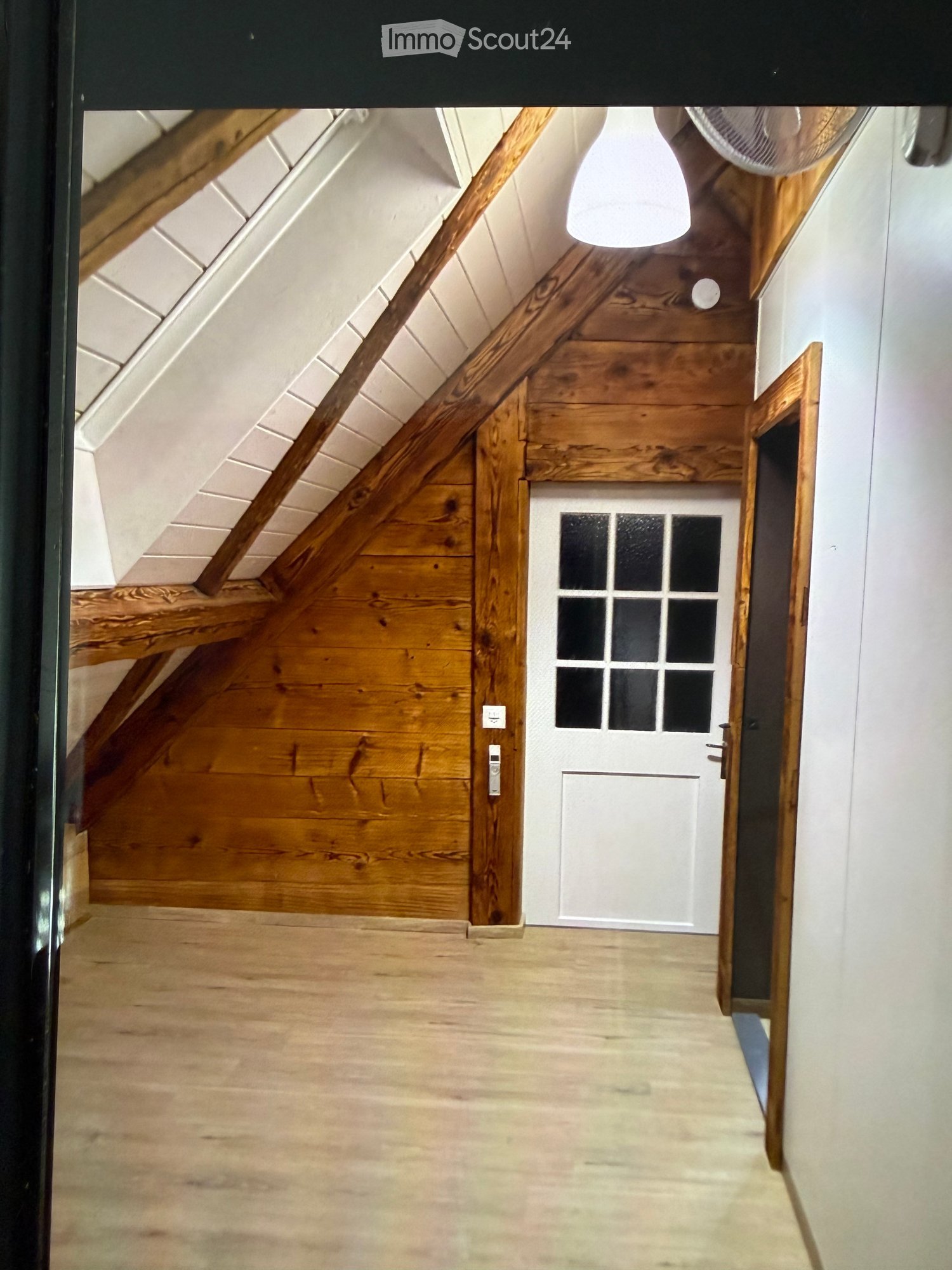 Wooden staircase leading up, white door with glass panels, wooden walls, and exposed wooden beams on the ceiling.