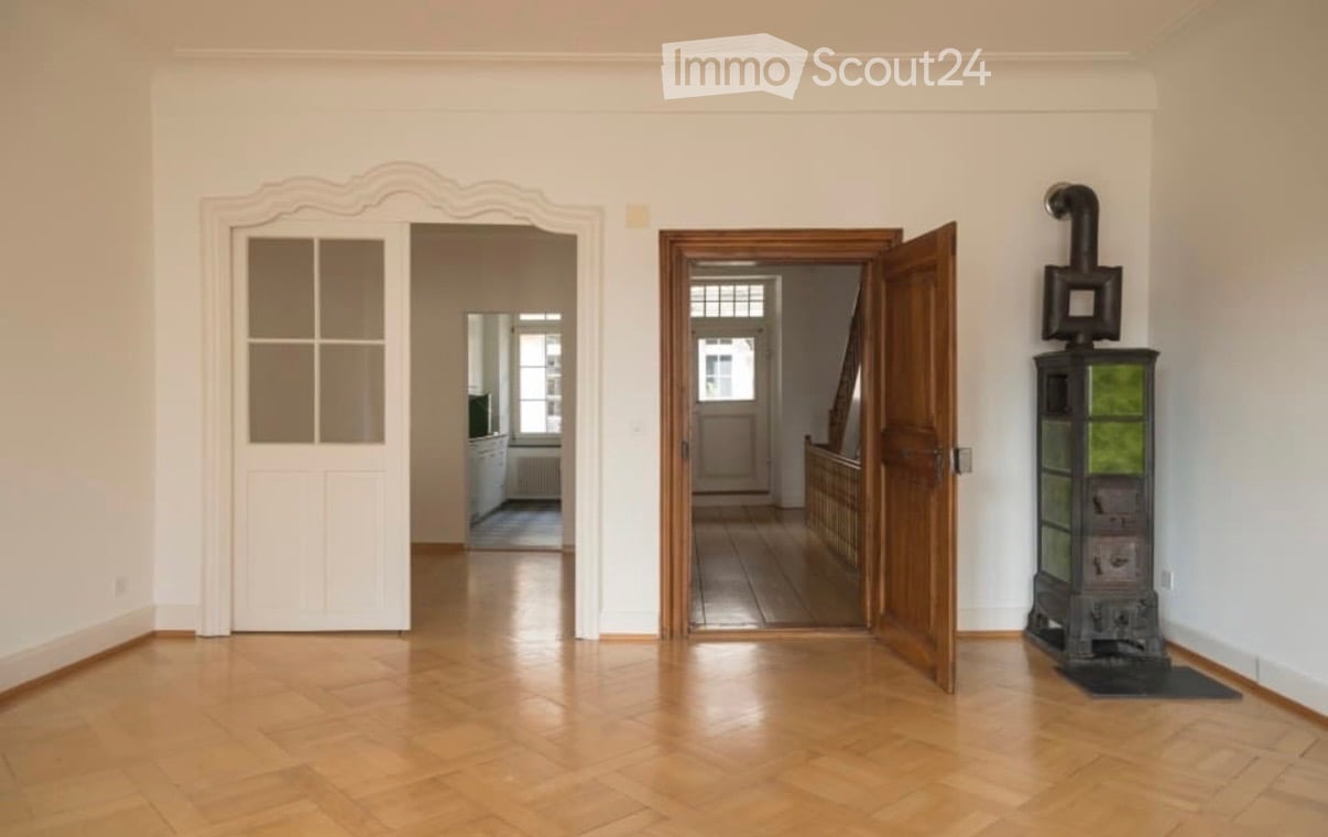Empty hallway with wooden flooring, white walls, and two open doors leading to other rooms. A decorative stove is visible on the right side.