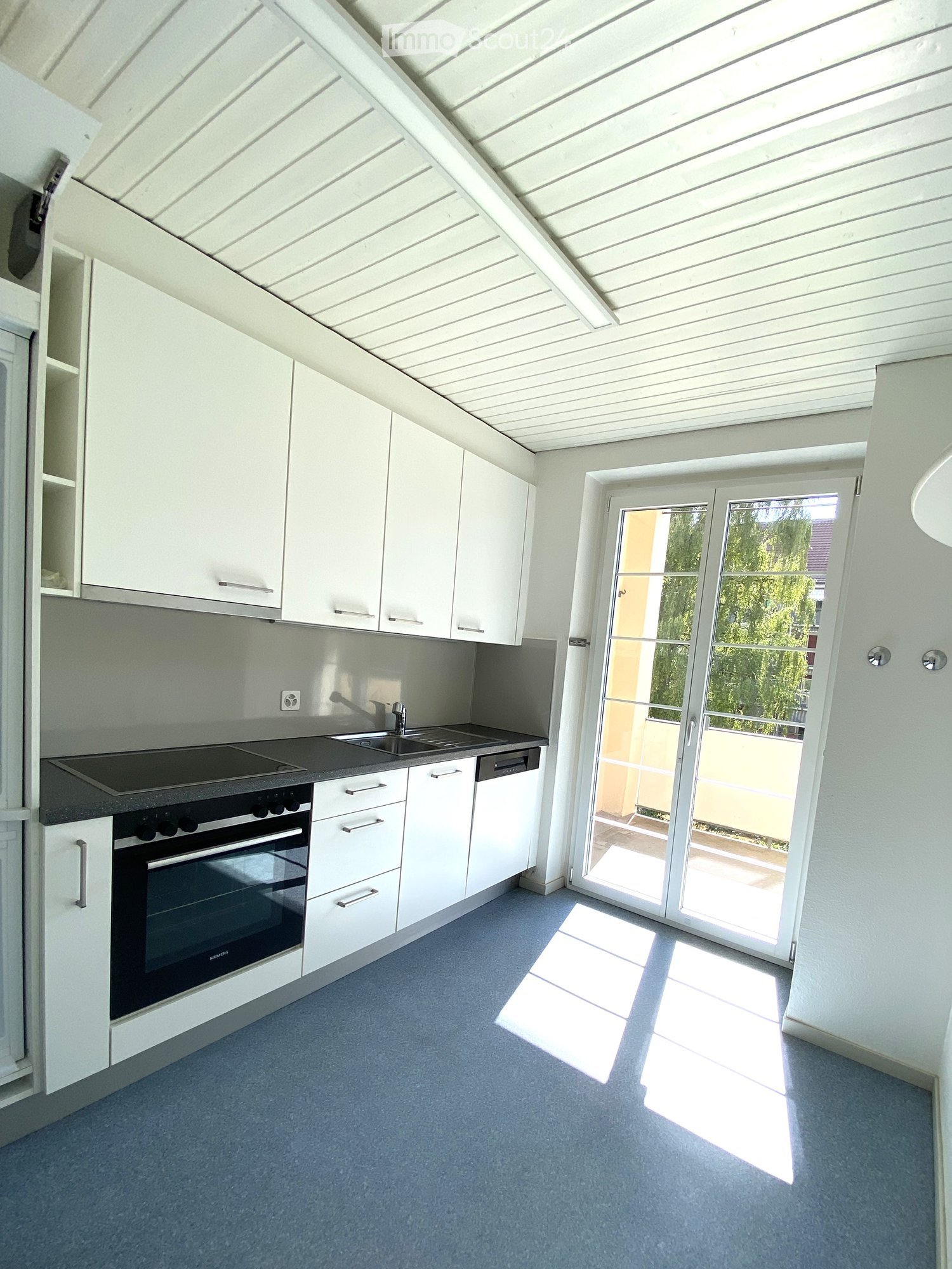 Modern kitchen with white cabinets, stainless steel appliances, and a large sliding glass door leading to a balcony.