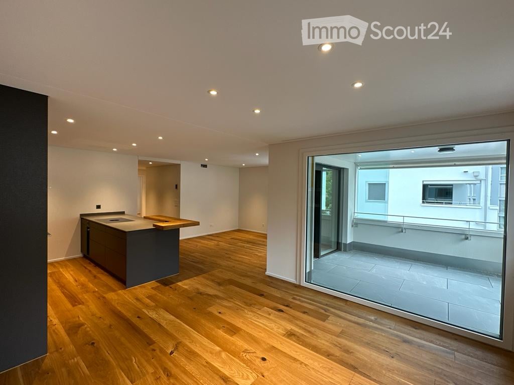 Modern kitchen with wooden flooring, a kitchen island, and a large sliding glass door leading to a balcony.