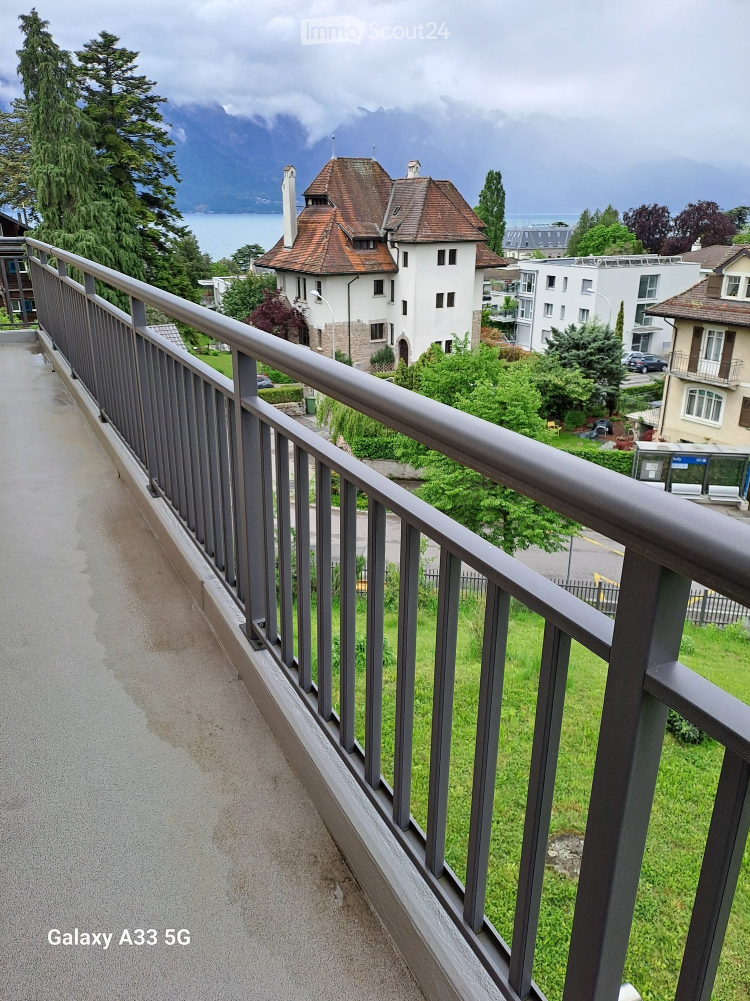 Balcony overlooking a scenic view of a lake and mountains, with a metal railing and a pathway leading down.