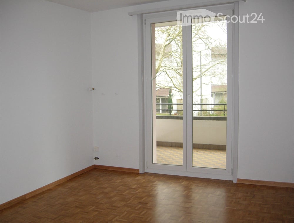 Empty room with wooden flooring, white walls, and a large sliding glass door leading to a balcony.