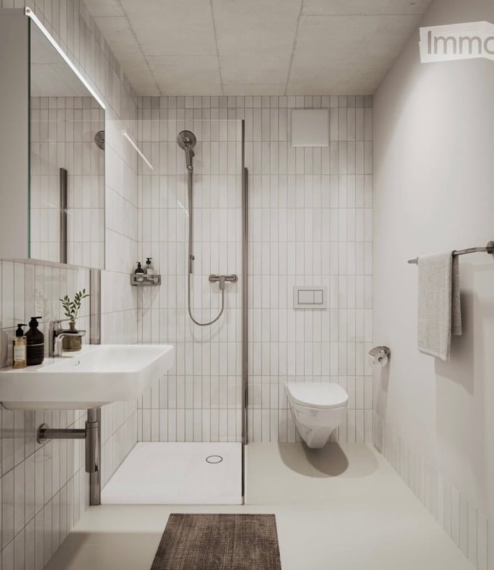 Modern, minimalist bathroom with white tiles, a corner shower, a sink with a mirror, a toilet, and a small plant on the sink counter.