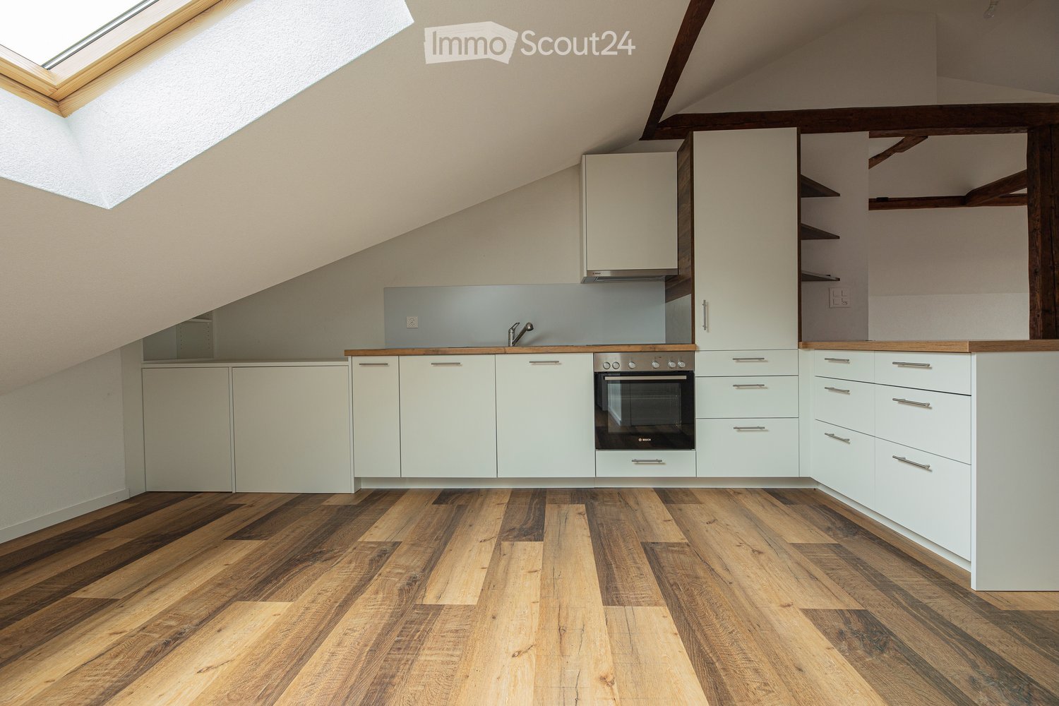 Modern kitchen with white cabinets, wooden countertops, and a built-in oven. Features a skylight window and wooden flooring.