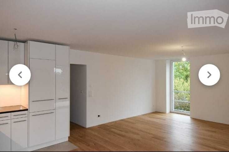 Bright, modern kitchen with white cabinets, a sleek countertop, and a large window leading to a balcony. The floor is made of polished wood.