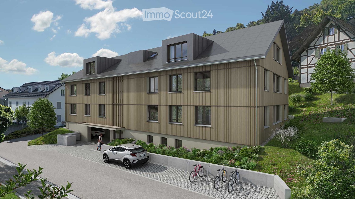 Modern two-story building with a garage, multiple windows, and a sloped roof. The surrounding area includes a driveway, parked car, and bicycles.