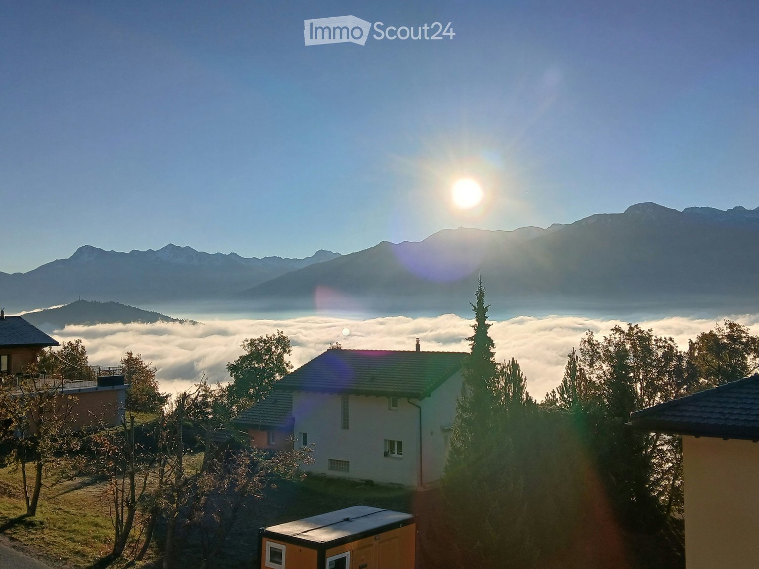 A serene mountain view with a house nestled among trees, surrounded by a sea of clouds and distant peaks.