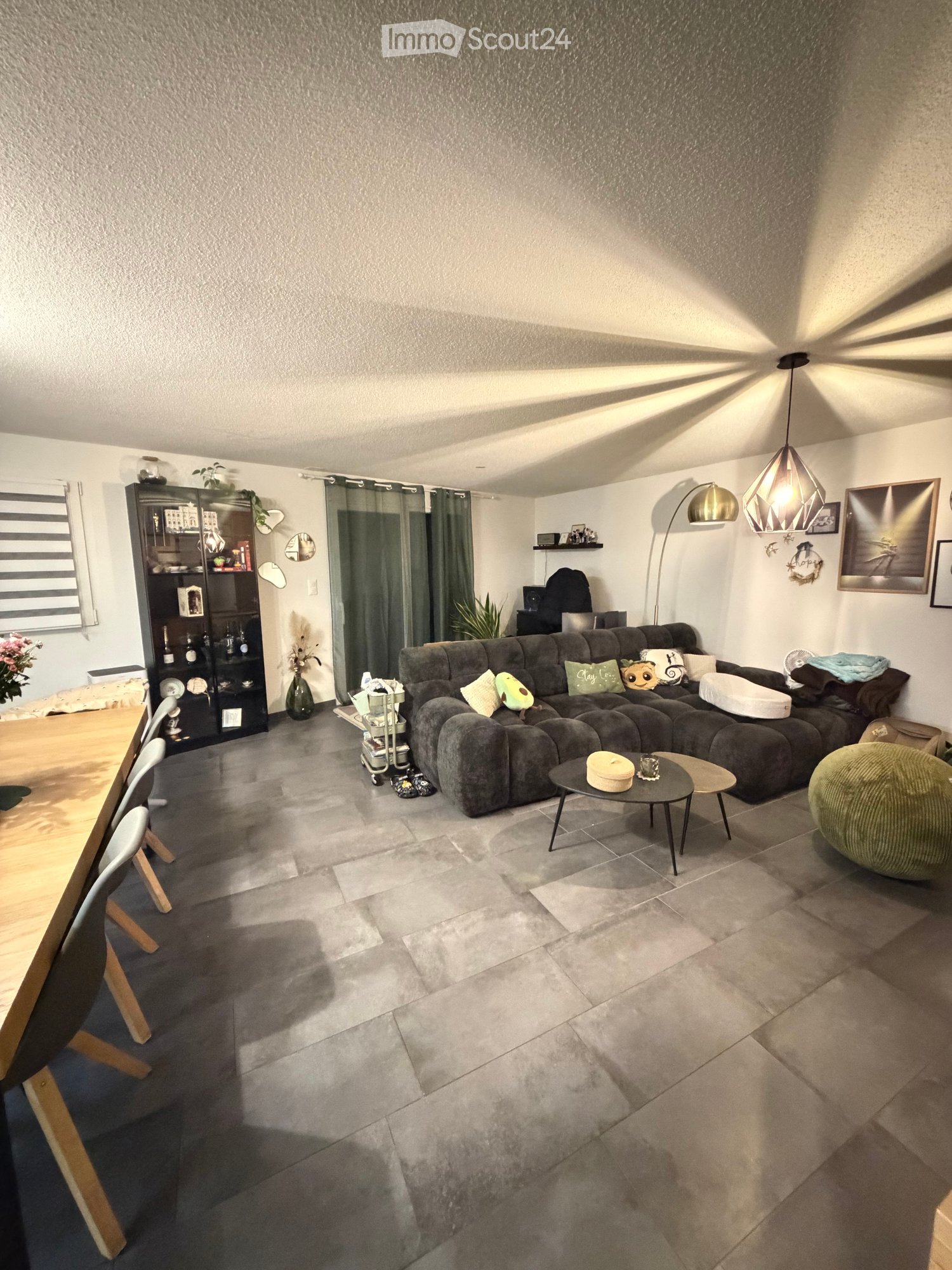 Modern living room with grey sectional sofa, coffee table, dining table, chairs, shelf, floor lamp, and decorative items.