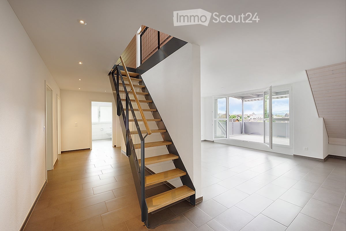 Modern hallway with wooden stairs, white walls, and large windows leading to a balcony with a scenic view.