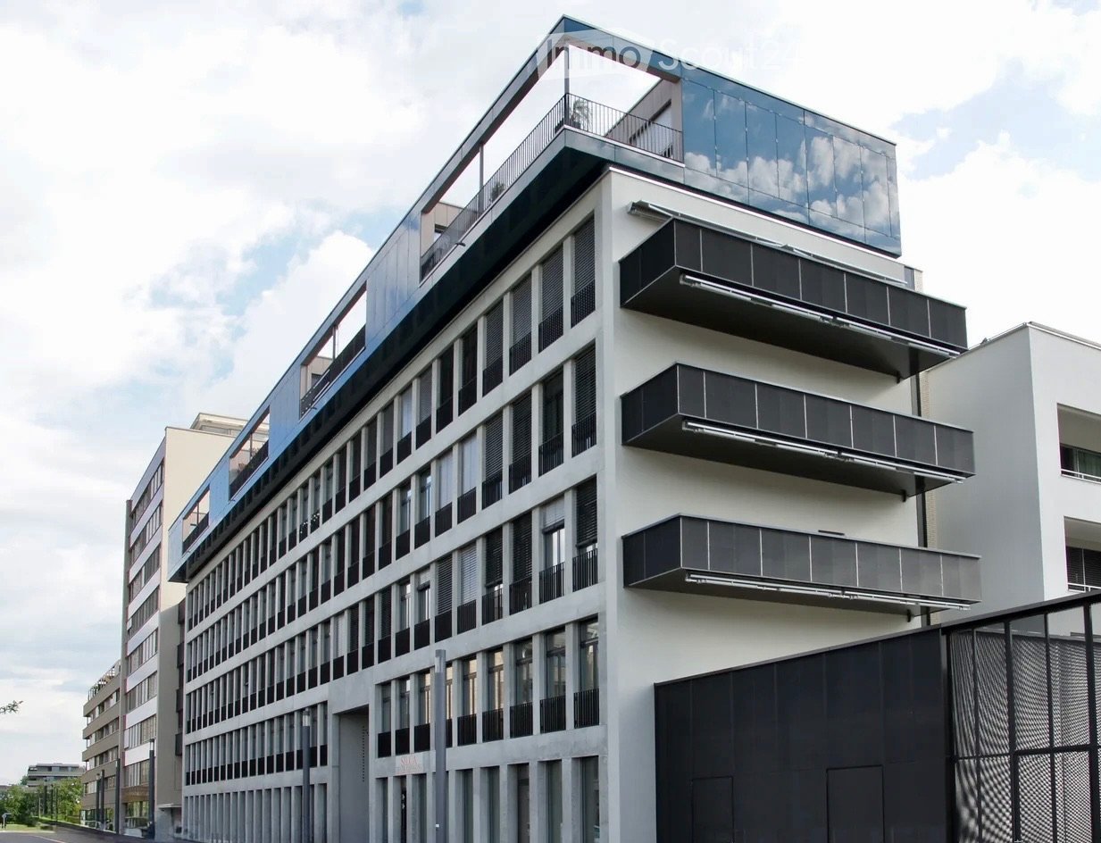 Modern multi-story building with large windows, balconies, and a sleek design.