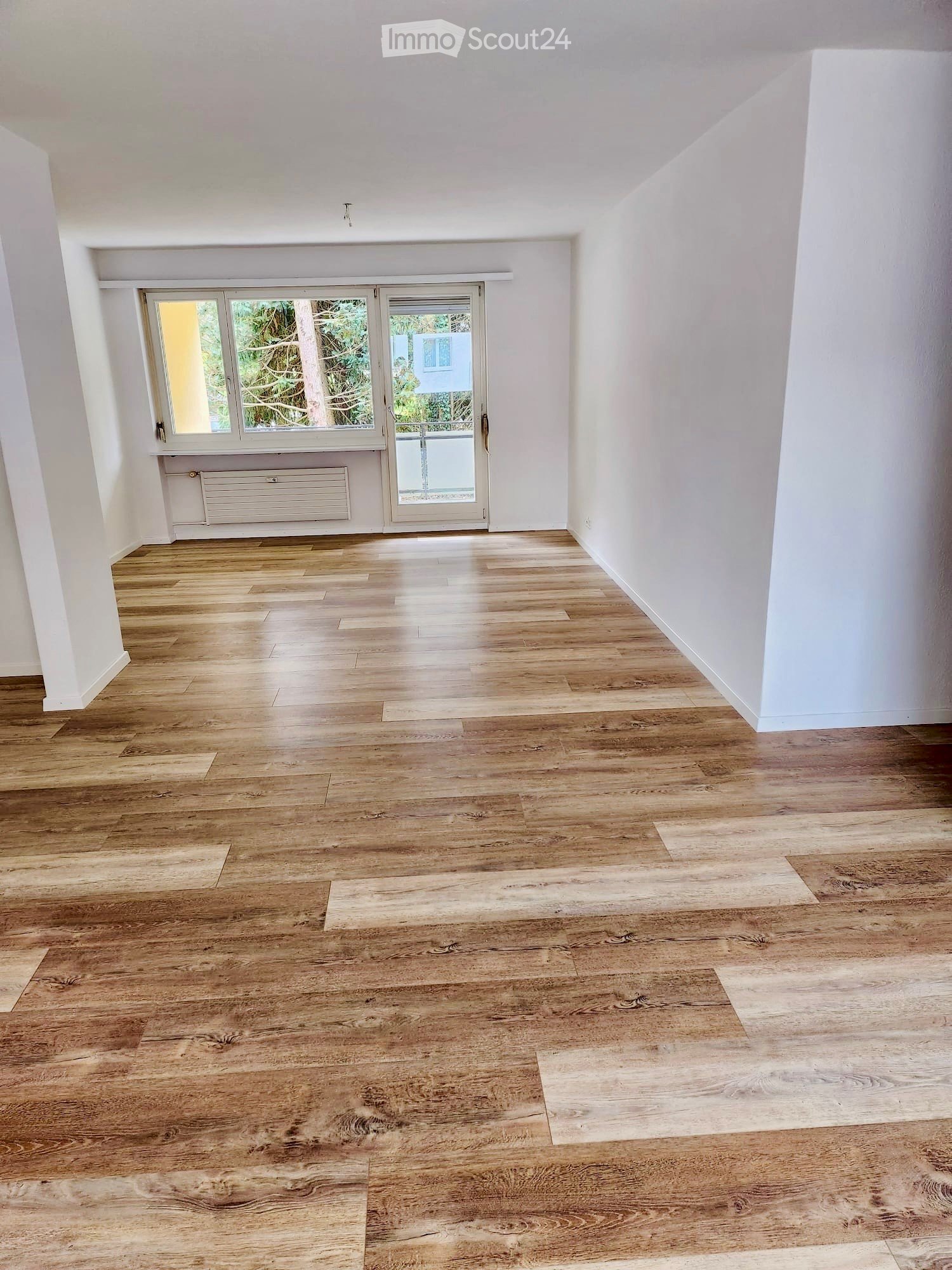 Empty room with wooden flooring, white walls, large window, and sliding glass door leading outside.