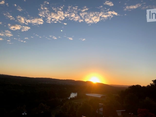 Scenic view of a sunset over a valley with a river and distant hills, with a small structure visible in the foreground.