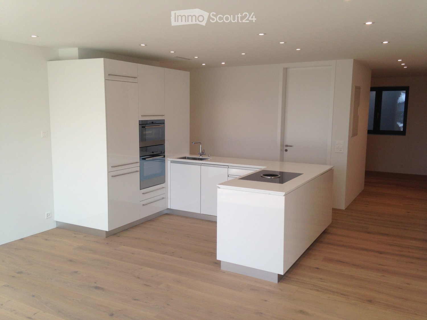 Modern kitchen with white cabinets, a central island, an induction cooktop, and a sink with a faucet. The floor is made of light wooden planks.