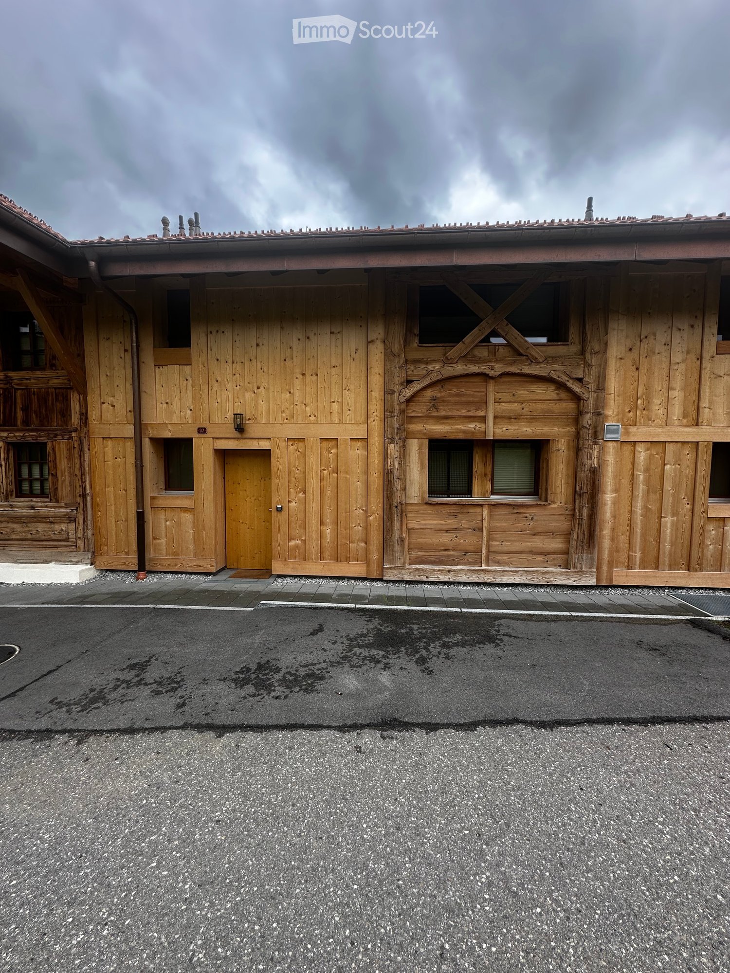 Wooden building with a tiled roof, large wooden doors, and windows, featuring a small entrance and a number sign on the wall.