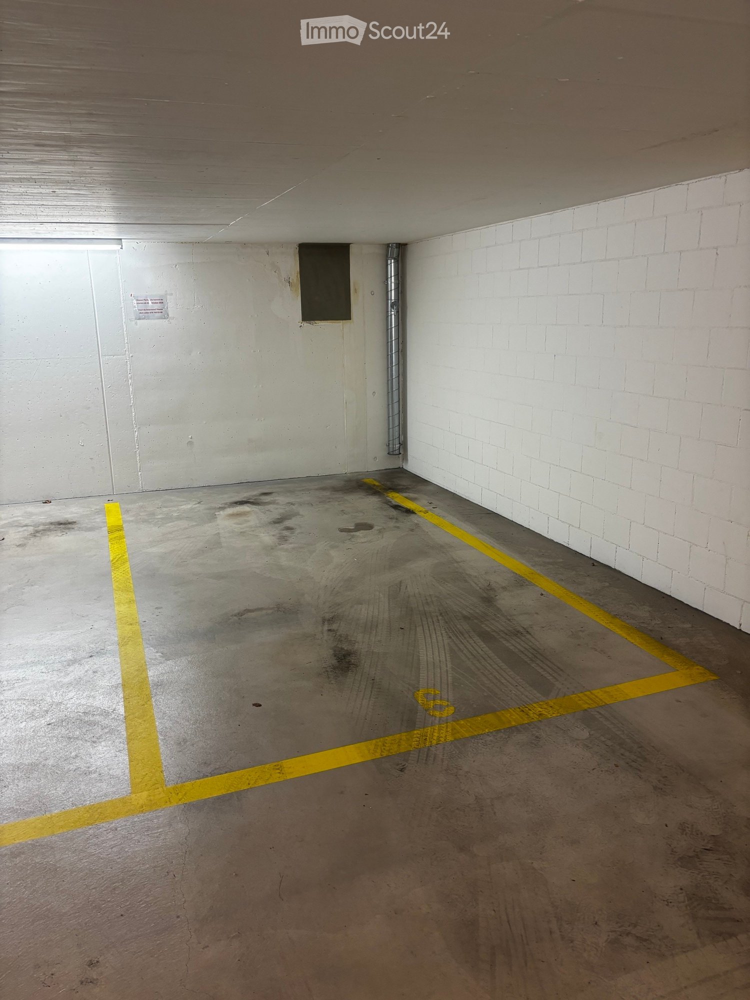 Empty underground parking space with concrete floor, white brick walls, and yellow parking lines.