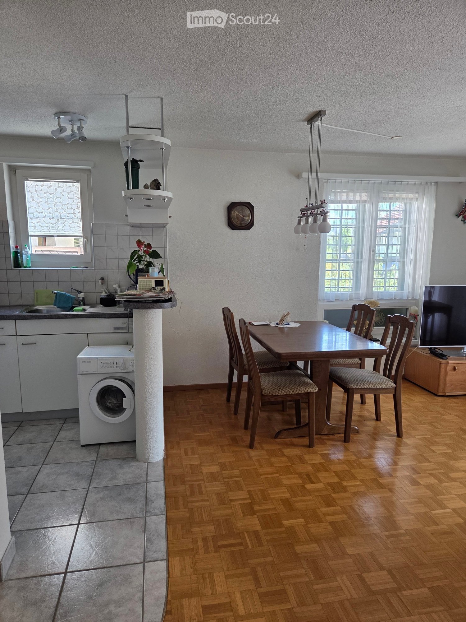 Open-plan kitchen and dining area with wooden flooring, a table with chairs, a washing machine, and a sink.