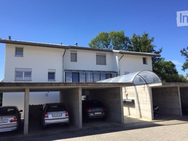 Two-story white building with a covered garage area containing three parked cars.