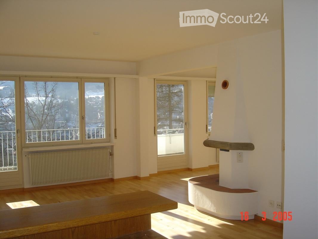 Empty room with wooden flooring, large windows, and a white fireplace structure. No furniture or equipment present.