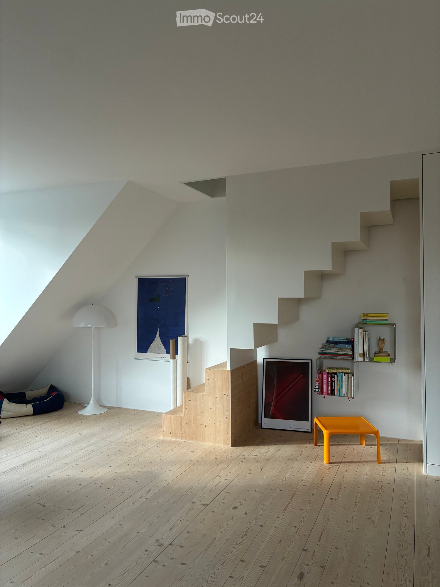 Attic room with wooden flooring, white walls, built-in shelves, a floor lamp, a small orange stool, and a dog bed in the corner.