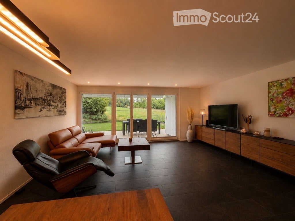 Modern living room with dark tiled flooring, large glass doors opening to a green outdoor area, leather sofa, coffee table, TV stand, and decorative vases.