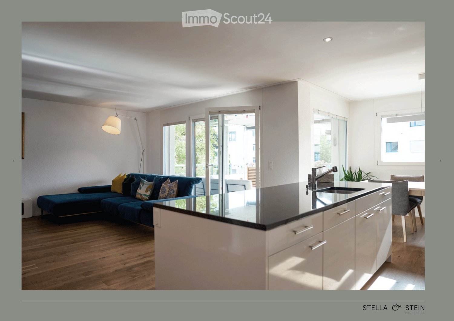 Open-plan living and kitchen area with a dark blue sofa, kitchen island, and modern fixtures.