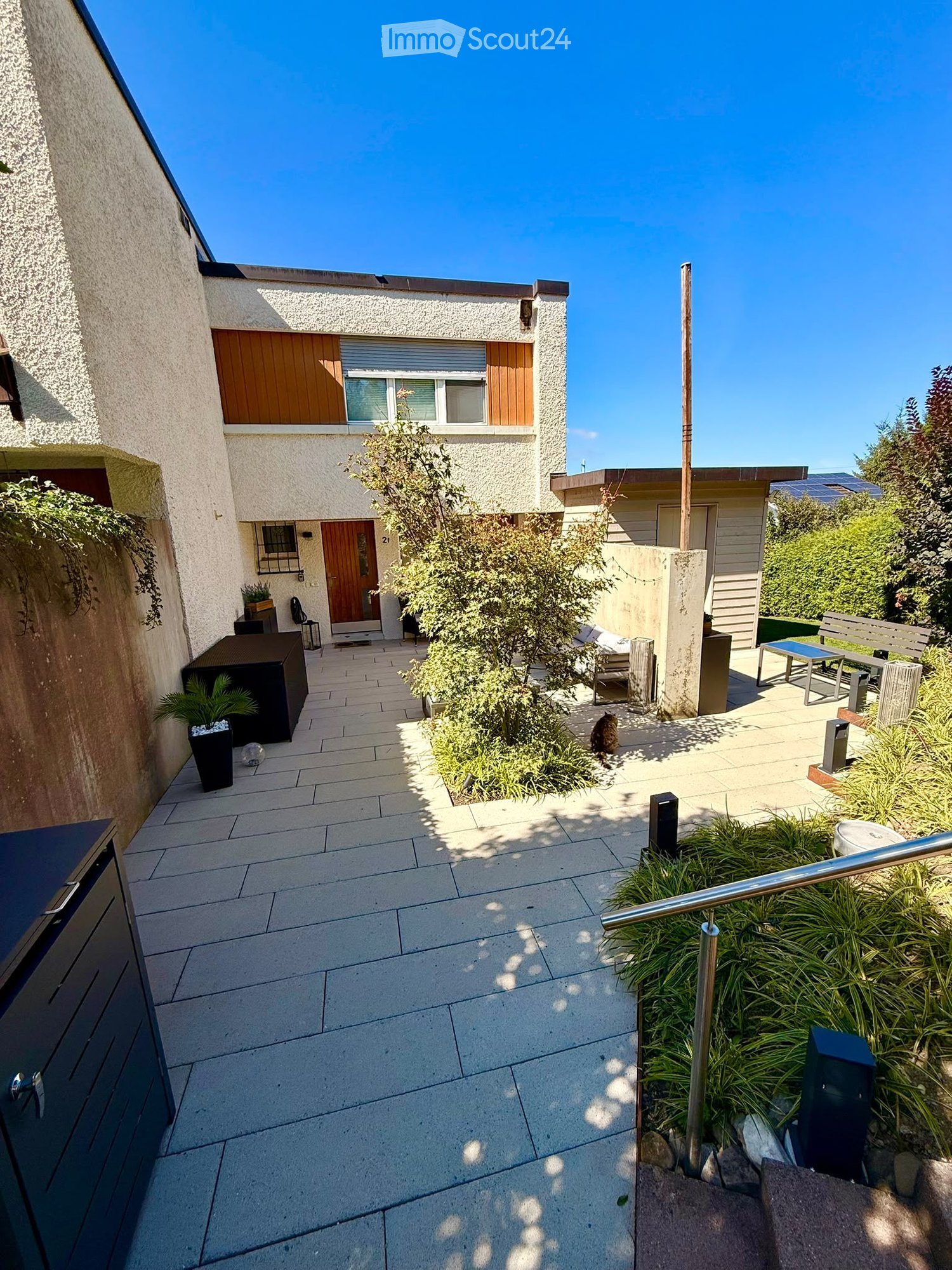 Courtyard with tiled pathway, small garden area, outdoor seating, and modern house entrance.