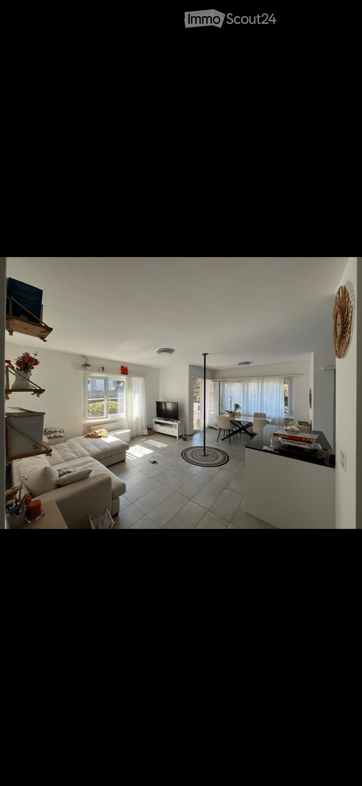 Bright living room with a large sofa, coffee table, TV stand, dining area with table and chairs, and decorative shelf with flowers.