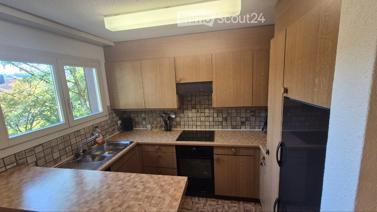 The kitchen features light wooden cabinets, a tiled backsplash, and a countertop with a sink, faucet, and small appliances. There is also an oven and refrigerator visible.