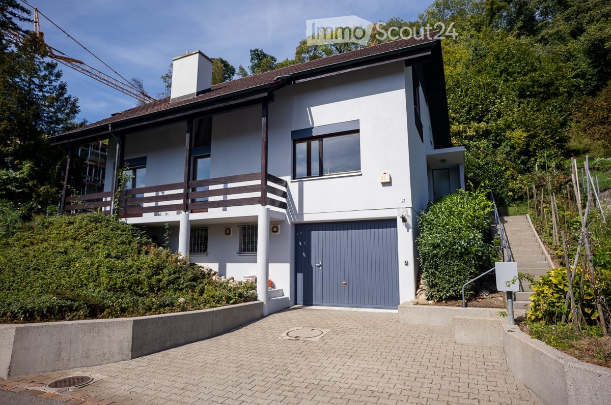 Two-story modern house with white exterior, grey garage door, and raised ground floor accessed by stairs.