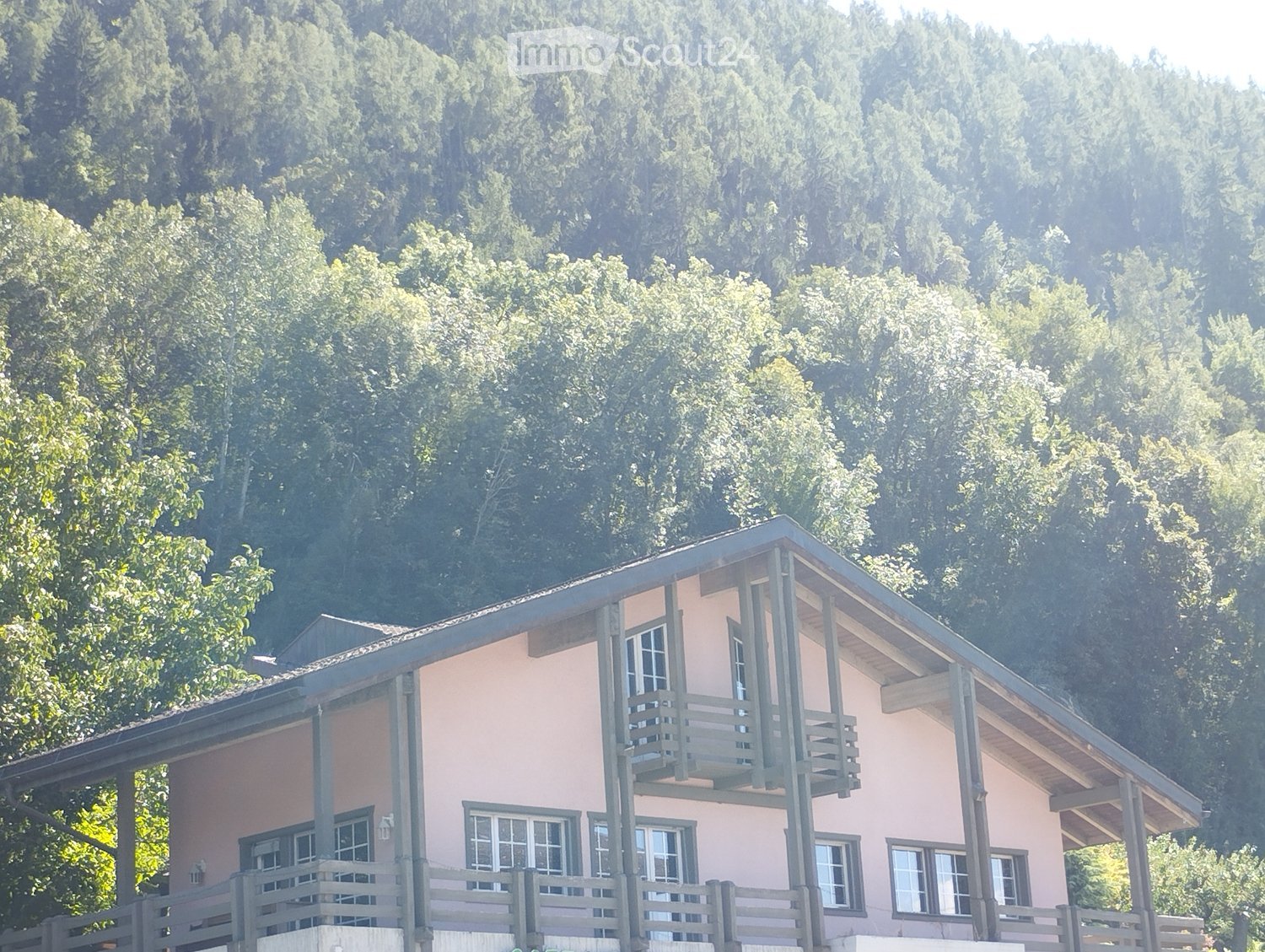Two-story house with pink exterior, multiple windows, and balconies overlooking a forested area.