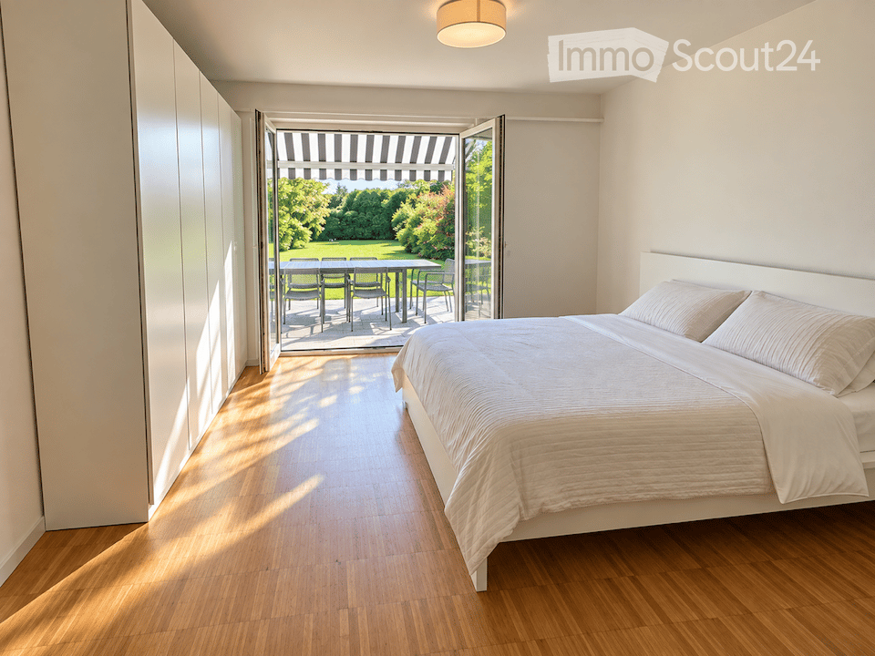 Modern bedroom with a large bed, white bedding, and a sliding glass door leading to a patio with outdoor furniture.