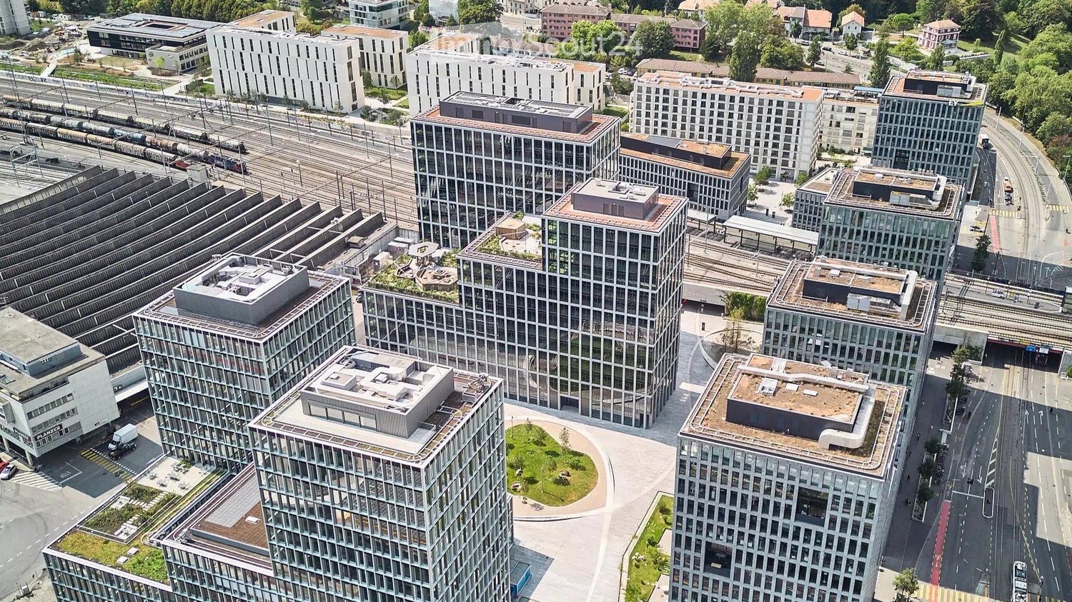 Aerial view of a modern urban development with multiple high-rise buildings, green spaces, and transportation infrastructure.