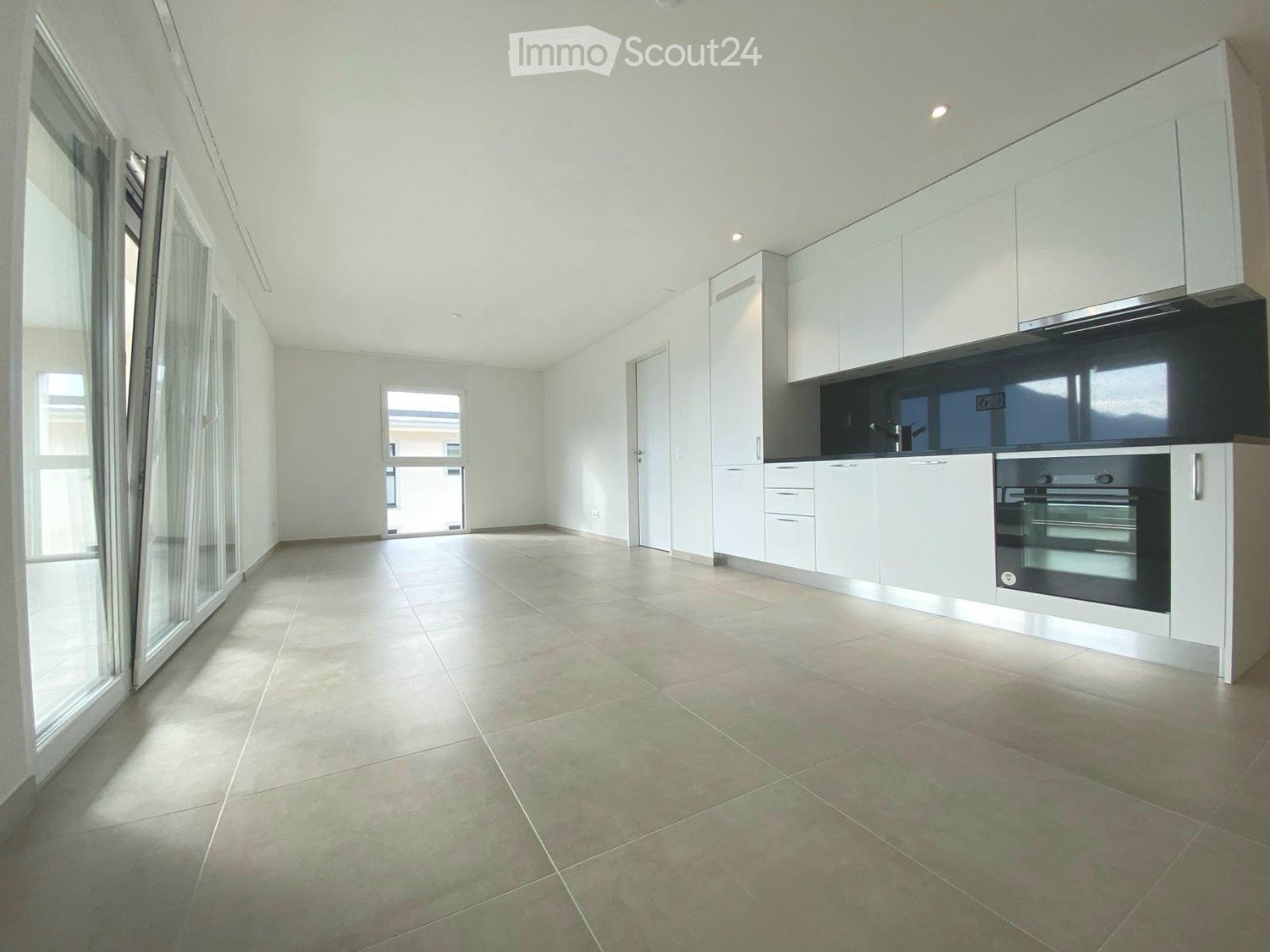 Modern kitchen with white cabinets, stainless steel oven, tiled floor, and large windows.