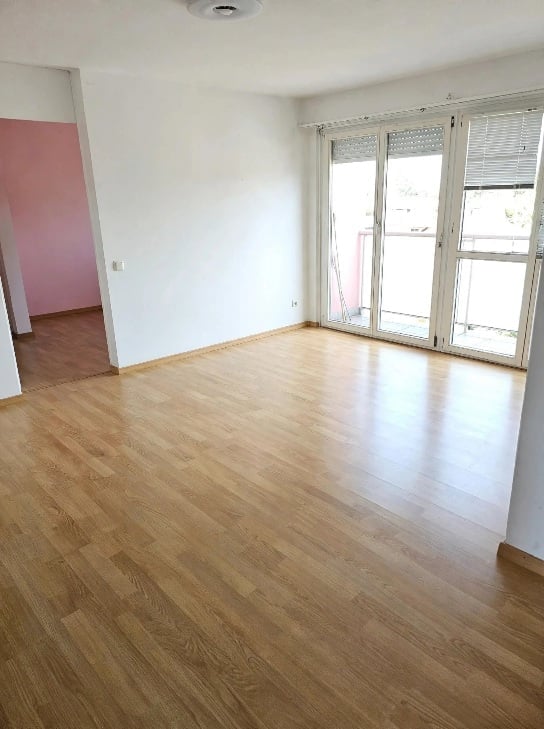 Empty room with wooden flooring, white walls, and large glass sliding doors leading to a balcony.