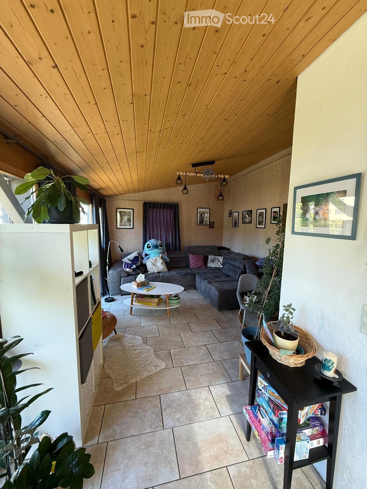 Living room with a grey sectional sofa, coffee table, small round table, and various decorative items including plants and picture frames.