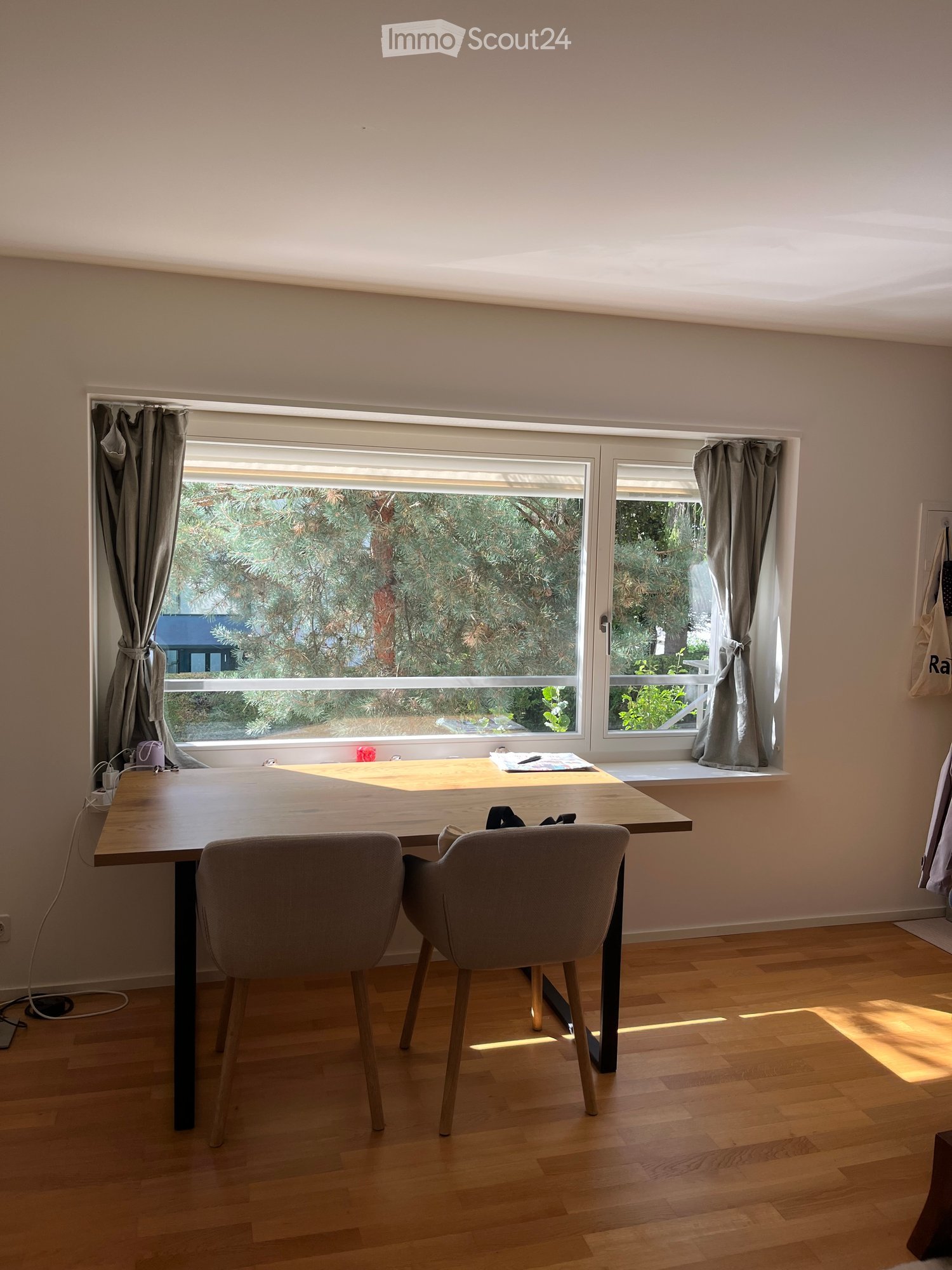 Bright room with wooden floor, large window with curtains, and a small table with two chairs.