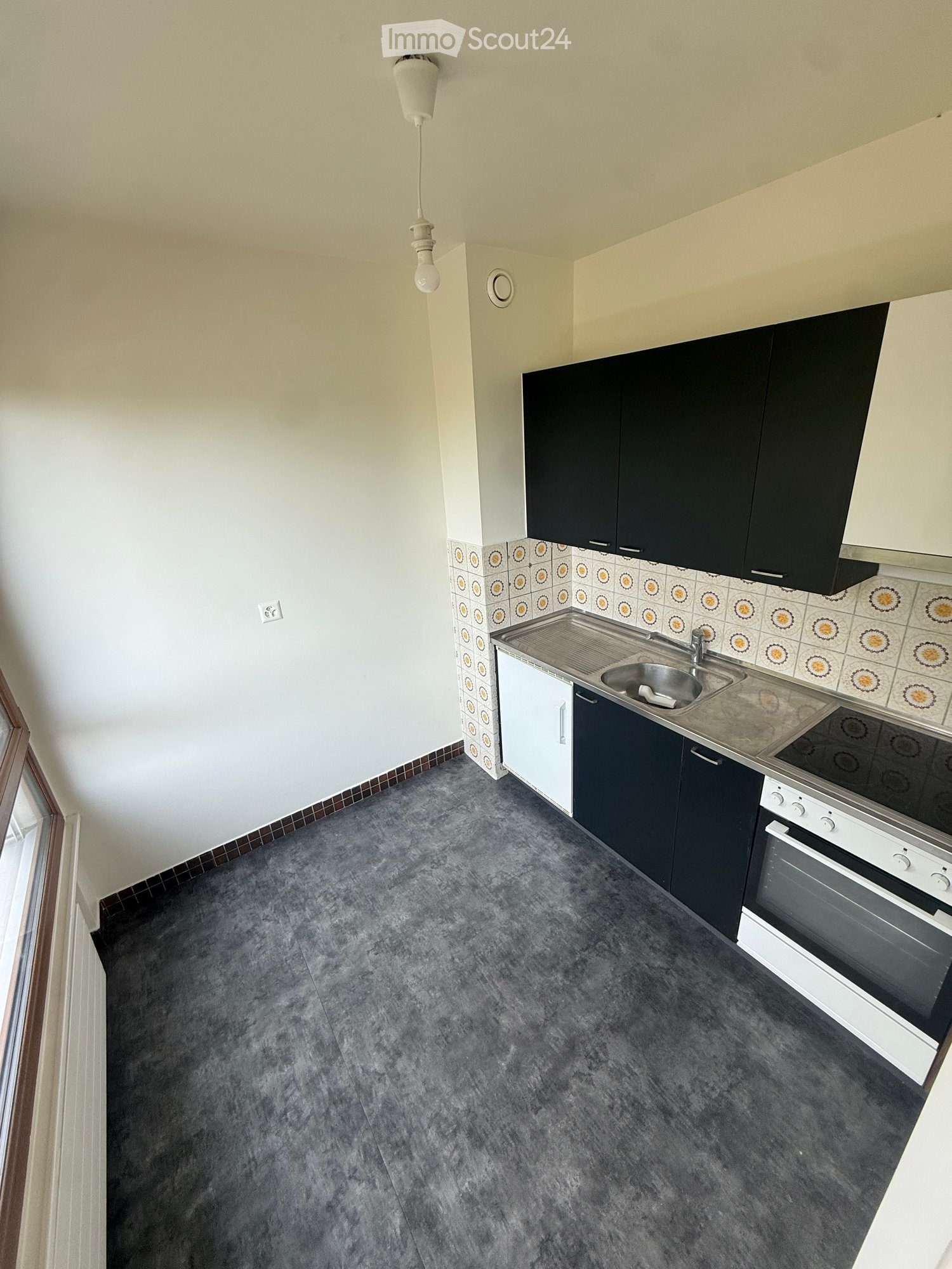 Modern kitchen with dark cabinets, stainless steel sink, and oven. Grey tiled floor and white walls.