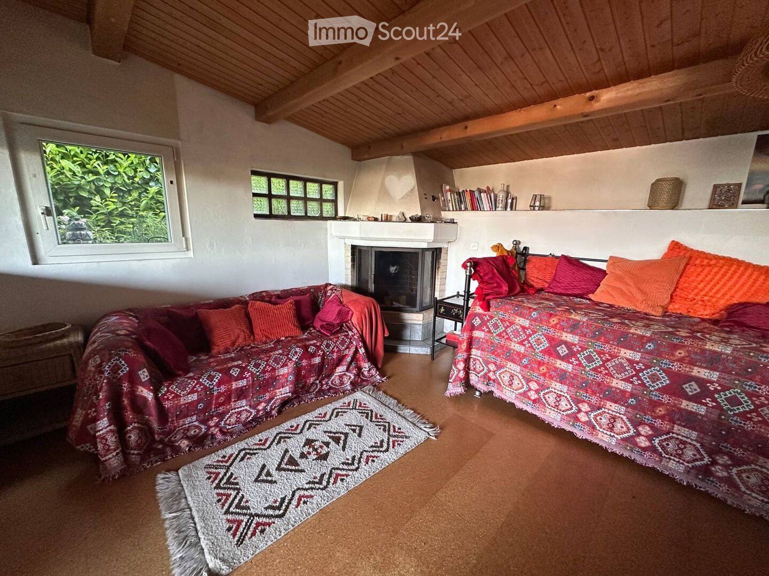 Cozy living space with a wooden ceiling, fireplace, sofa, daybed, and bookshelf.
