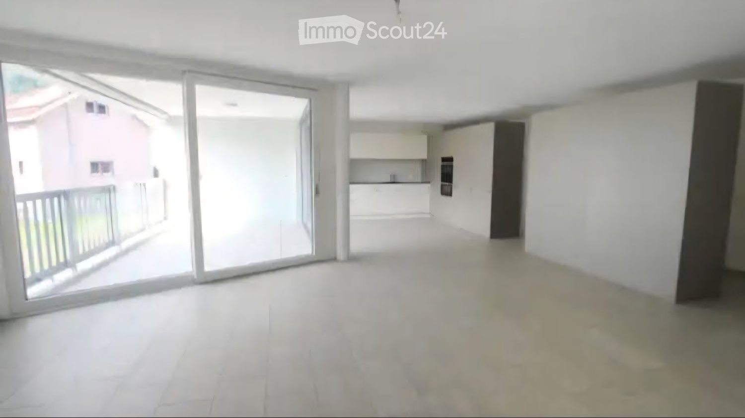 Empty living space with white walls, large sliding glass doors leading to a balcony, and a view of a neighboring building.