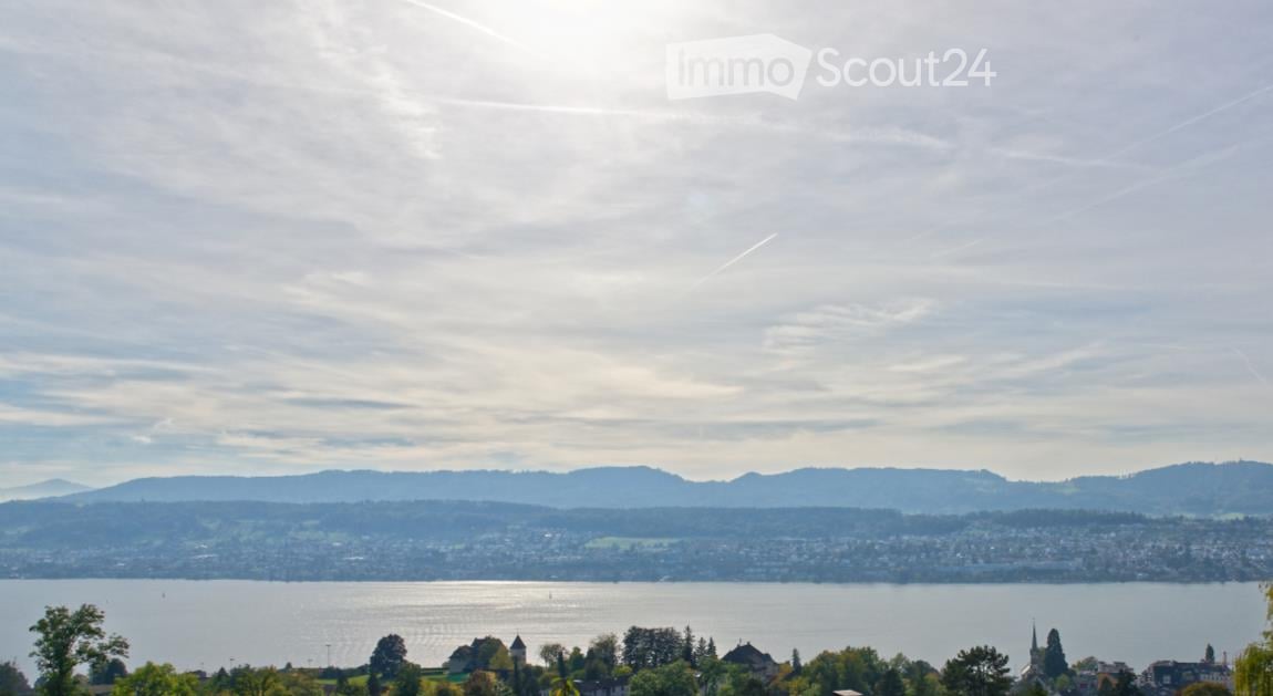 Panoramic view of a cityscape across a lake with distant mountains under a partly cloudy sky.