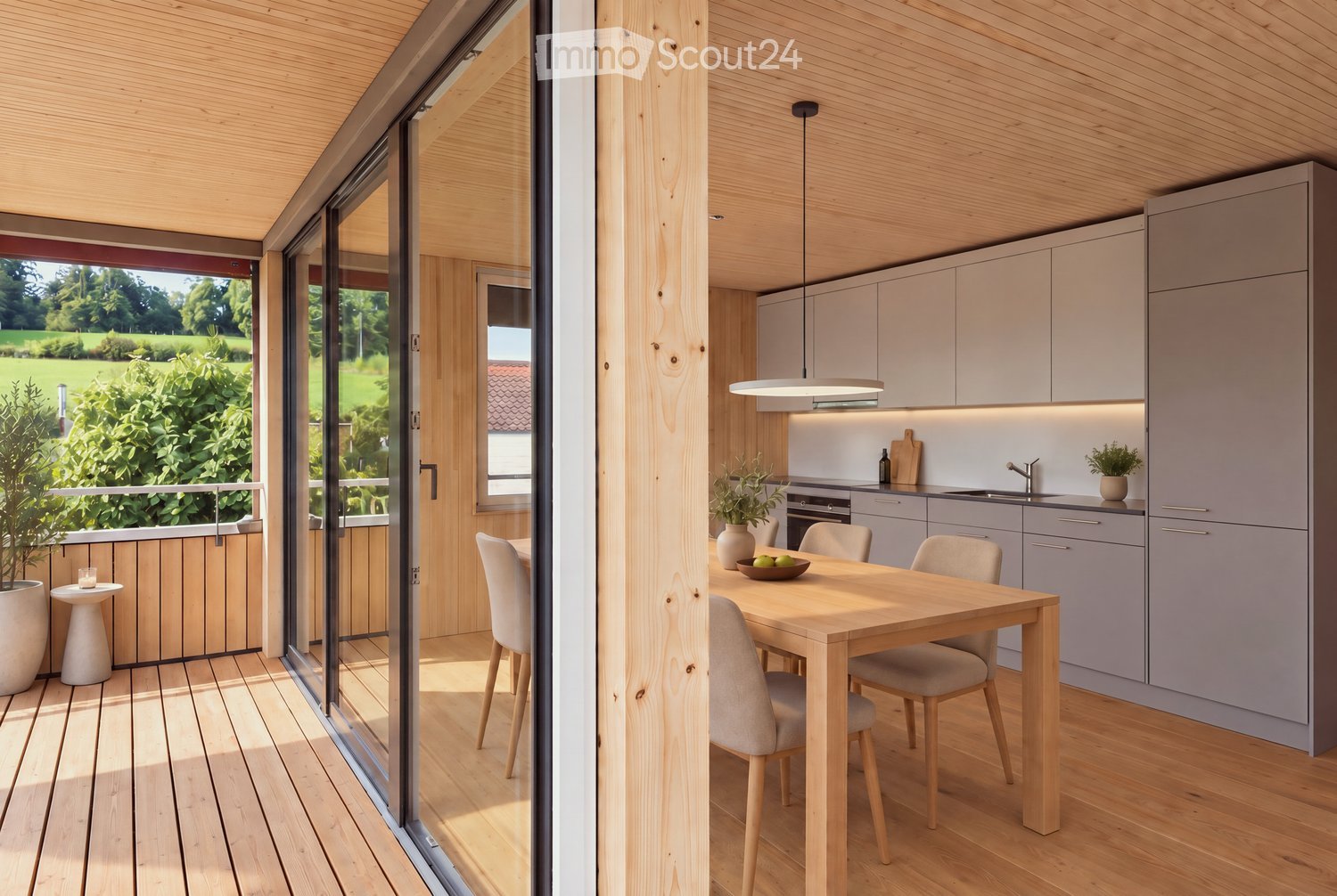 Modern kitchen with grey cabinets, wooden dining table, and chairs. Large sliding glass doors open to a wooden deck with outdoor seating and a view of a green landscape.