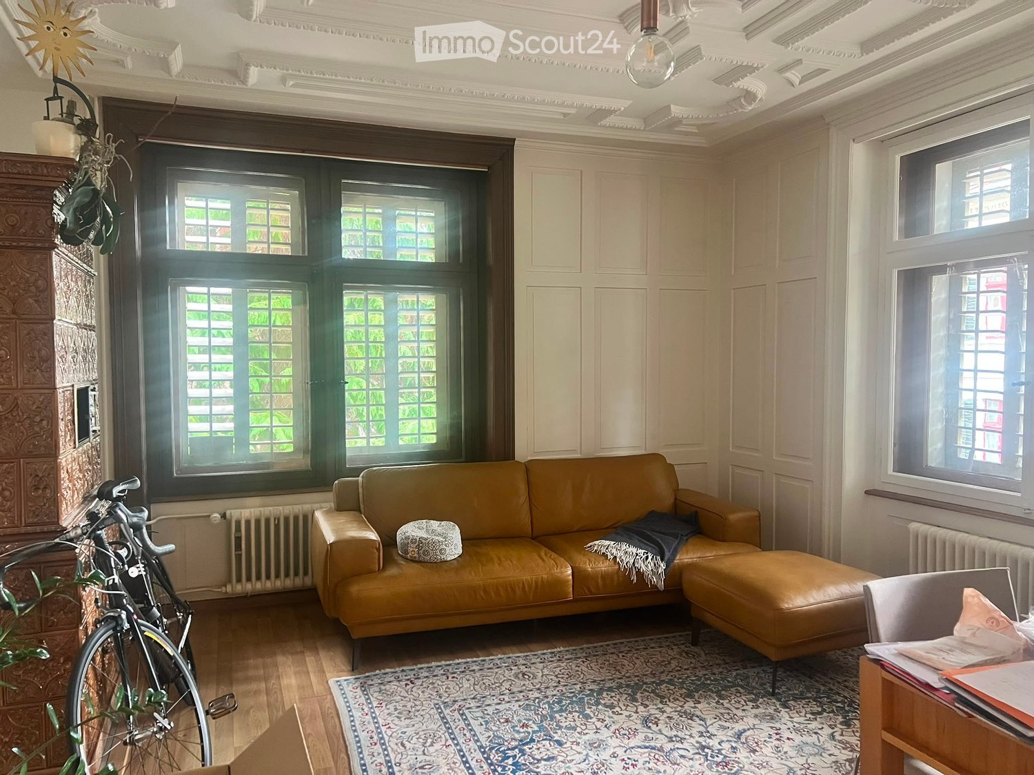 Living room with a tan leather sofa, ottoman, side chair, small table, bicycle, and patterned rug.