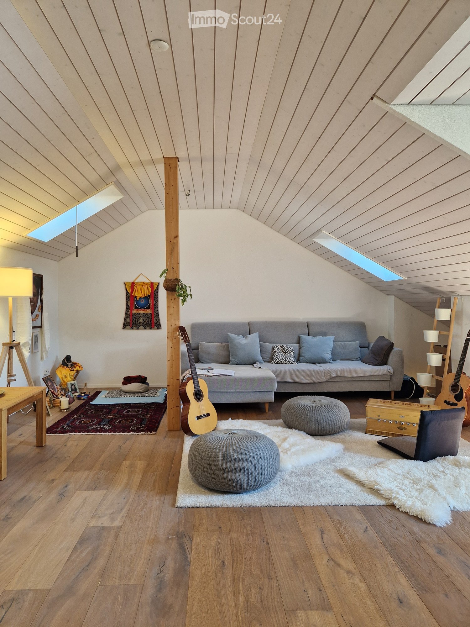 Living room with wooden floors, grey sofa, two round stools, guitar, small table, and decorative items.