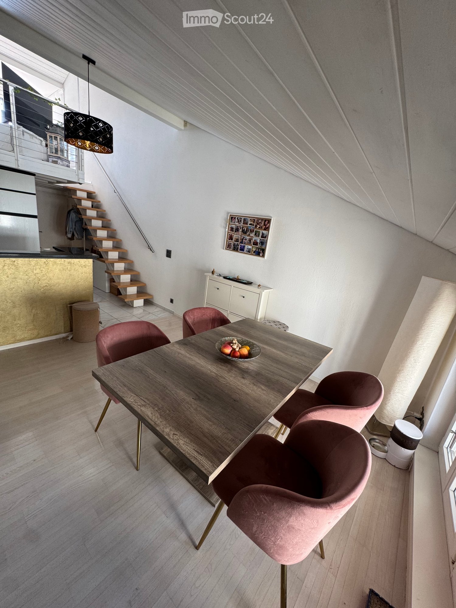 Dining area with a wooden table, pink chairs, a small cabinet, and a staircase leading to another level.