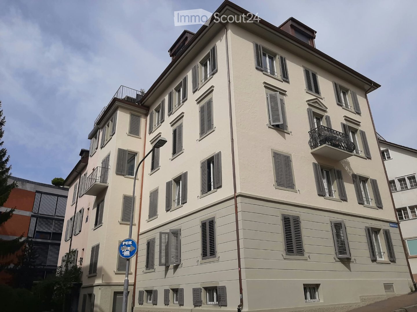 Four-story residential building with light beige facade, multiple windows with shutters, and balconies on upper floors.