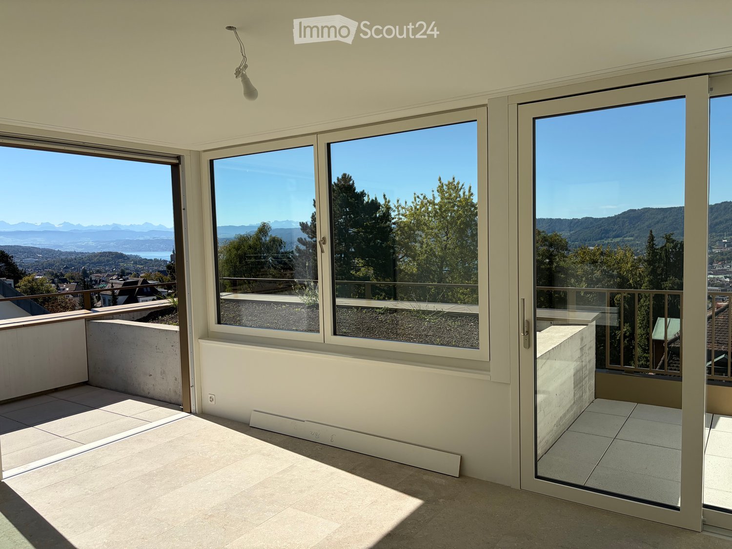 Bright, spacious balcony with large glass doors, tiled floor, and expansive scenic views of mountains and cityscape.
