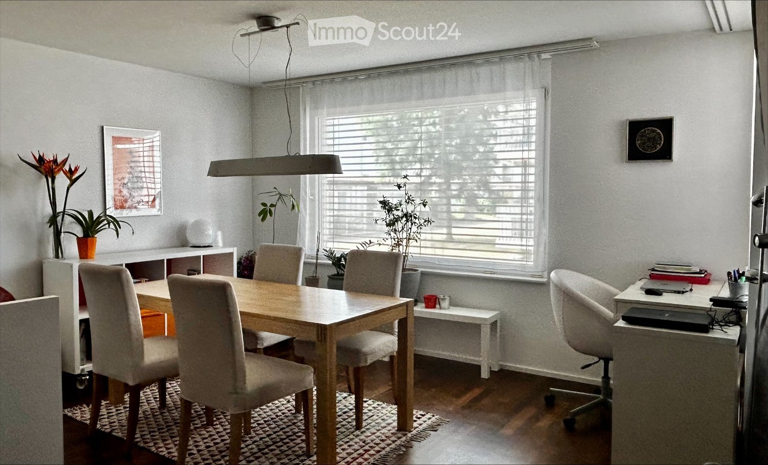 Bright dining and office area with a wooden dining table, six chairs, a desk with a laptop, and a hanging light fixture.